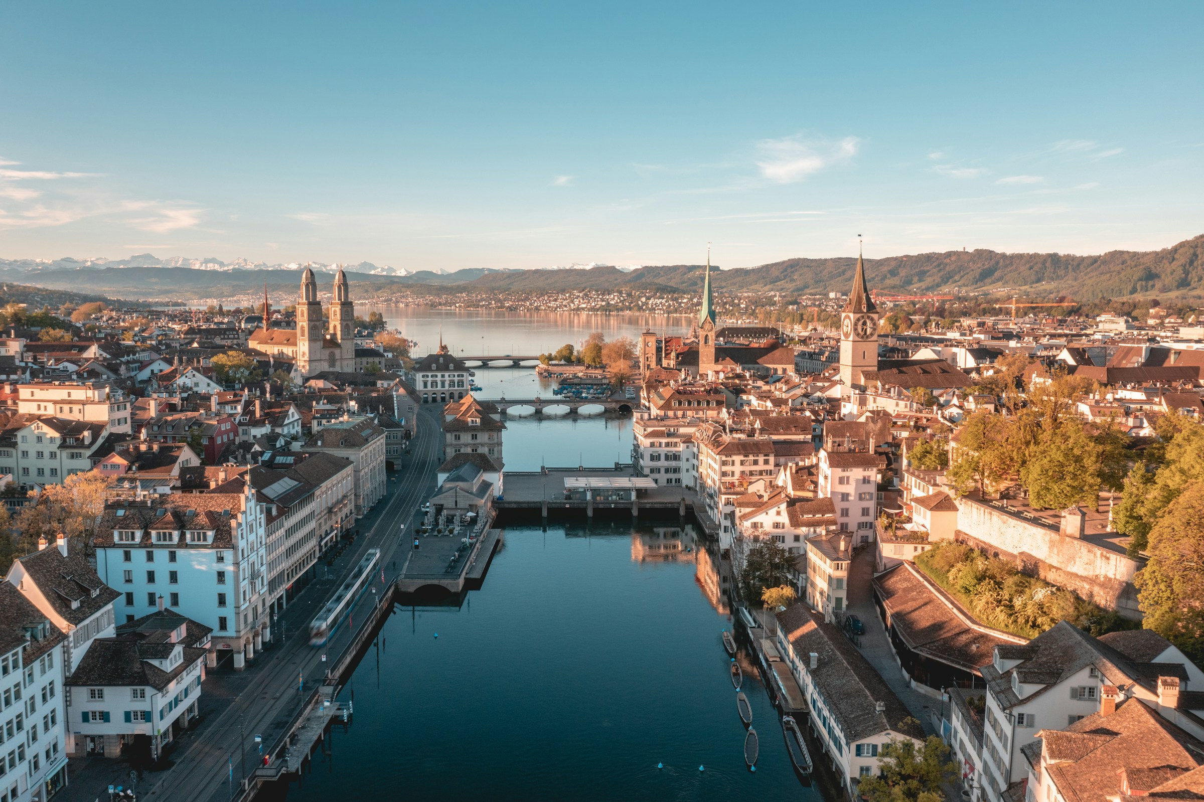 Die Limmat fließt durch die Stadt Zürich, umgeben von historischen Stadthäusern und modernen Gebäuden. Das Bild zeigt den Fluss im Stadtzentrum mit reflektierendem Wasser und einem urbanen Panorama aus Architektur und Uferwegen.